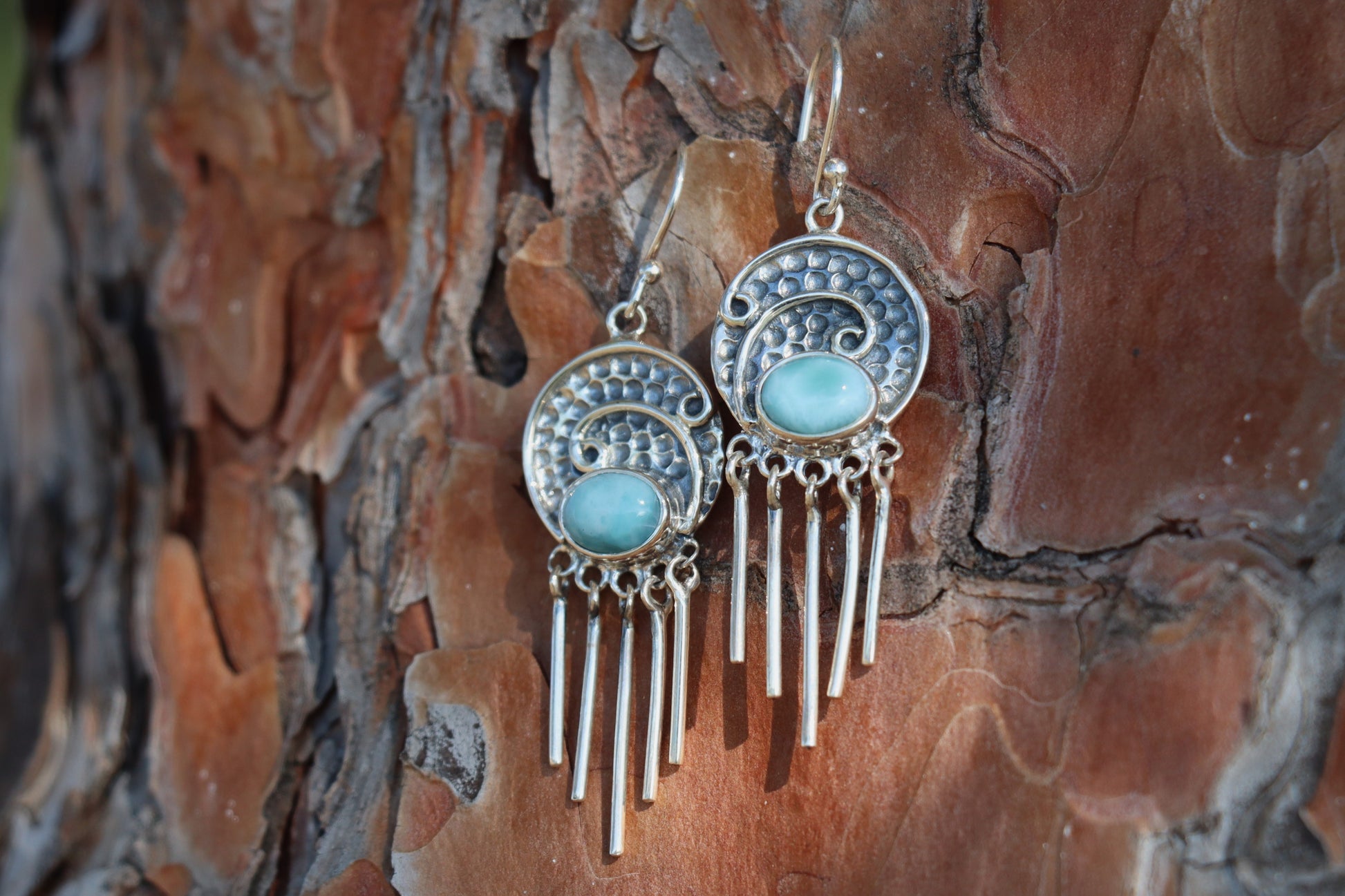 Angled shot of Larimar gemstone earrings with long silver fringe and ocean-blue stones, displayed on natural wood background. Handcrafted bohemian-style silver jewelry.