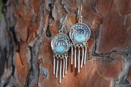 Angled shot of Larimar gemstone earrings with long silver fringe and ocean-blue stones, displayed on natural wood background. Handcrafted bohemian-style silver jewelry.