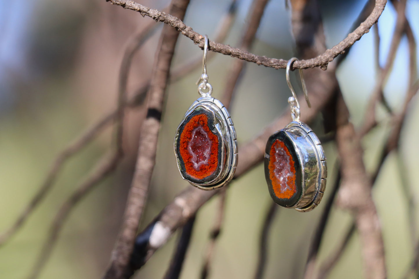 Pair of Tabasco Geode earrings displayed on a branch, featuring natural Mexican geode slices with bright orange outer rings and sparkling quartz centers. Handcrafted in sterling silver, symbolizing inner growth, emotional depth, and planetary alignment with Saturn and Pluto.