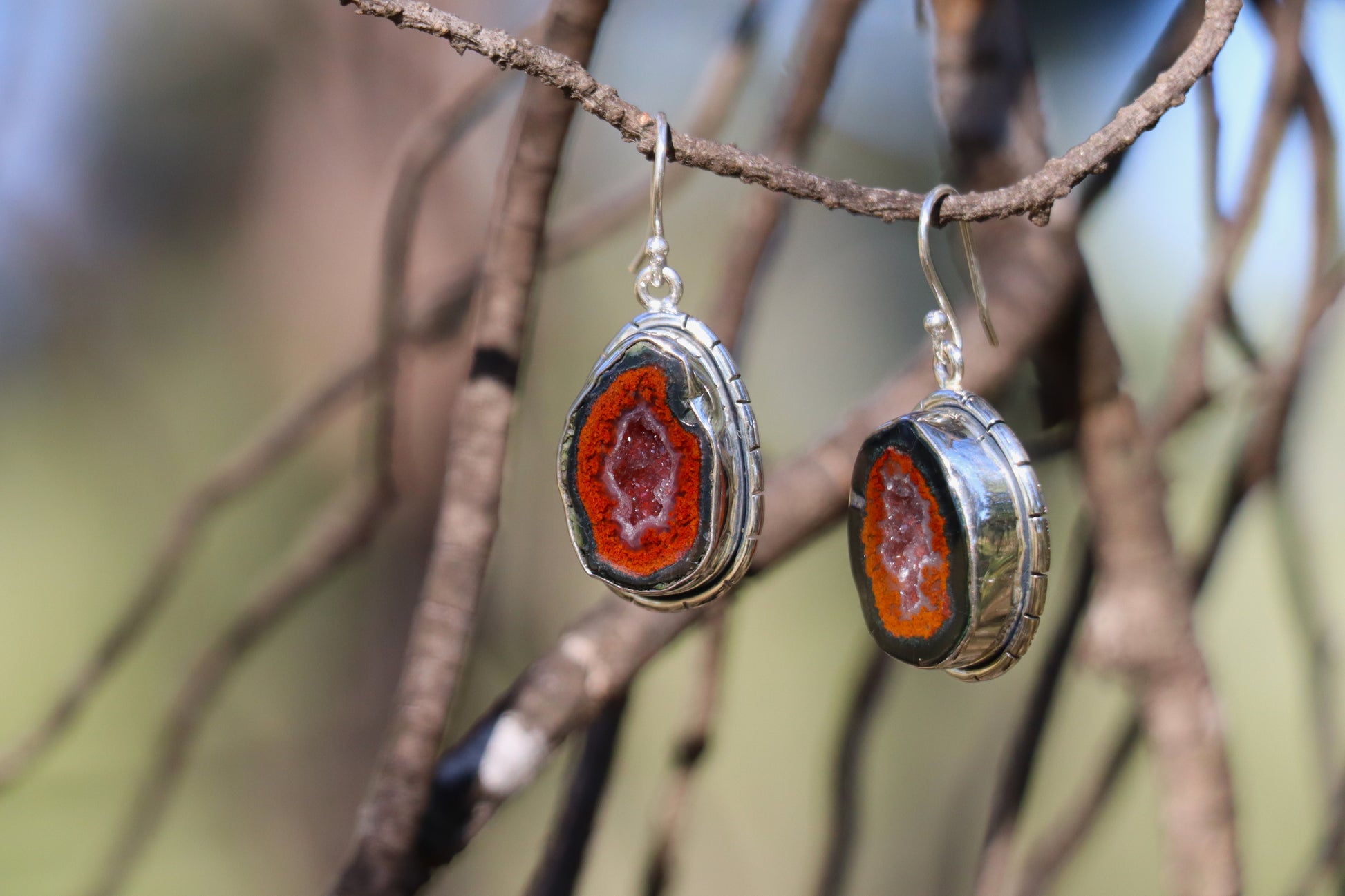 Pair of Tabasco Geode earrings displayed on a branch, featuring natural Mexican geode slices with bright orange outer rings and sparkling quartz centers. Handcrafted in sterling silver, symbolizing inner growth, emotional depth, and planetary alignment with Saturn and Pluto.