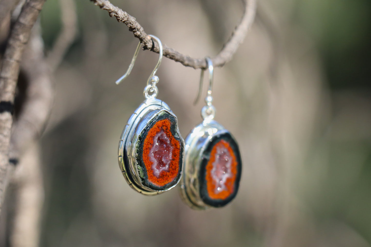 Tabasco Geode earrings photographed outdoors, showing their organic geode form, vibrant mineral layers, and polished sterling silver frame. A grounding, transformative stone supporting inner listening, shadow work, and spiritual integration.