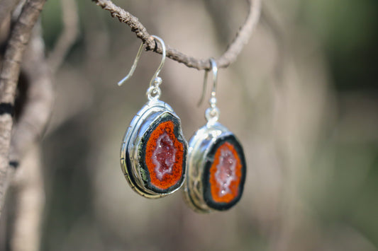Tabasco Geode earrings photographed outdoors, showing their organic geode form, vibrant mineral layers, and polished sterling silver frame. A grounding, transformative stone supporting inner listening, shadow work, and spiritual integration.
