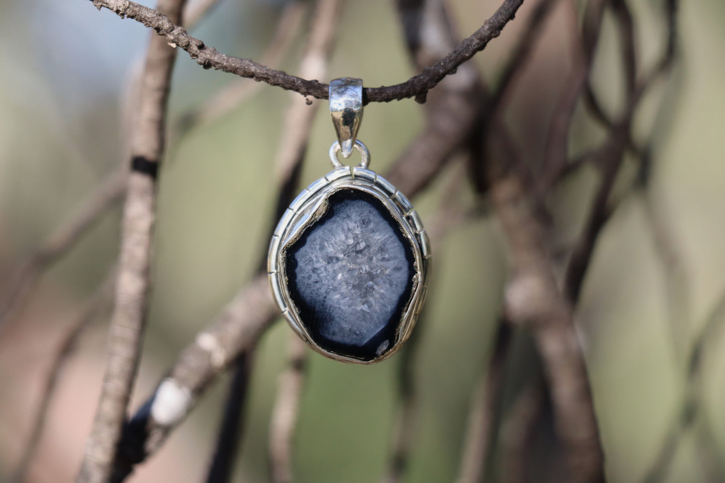 Oval coconut geode pendant with druzy quartz center in 925 sterling silver, displayed outdoors with soft natural lighting.
