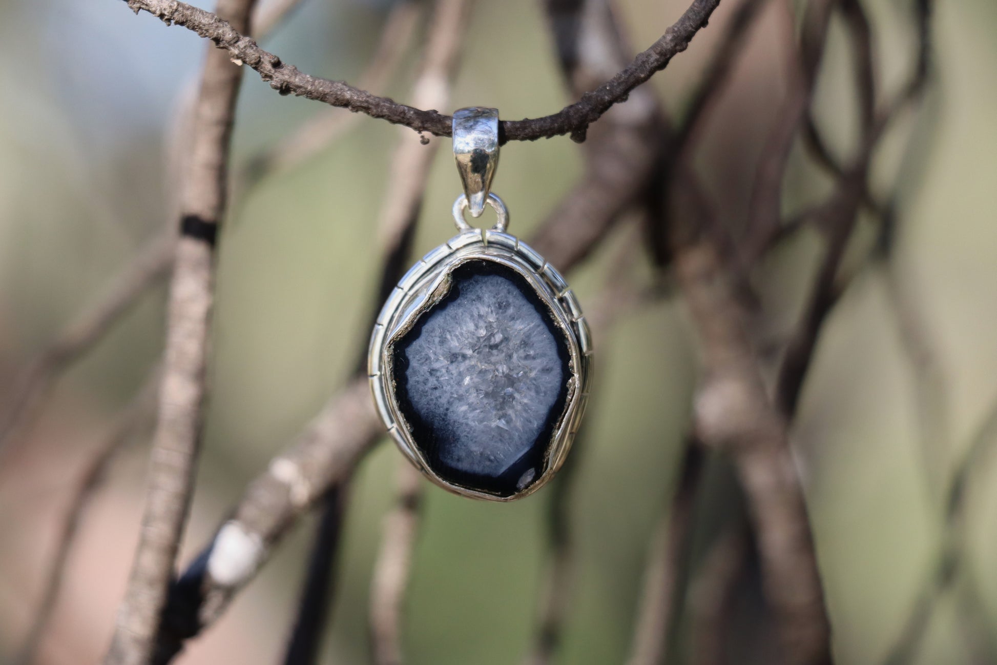 Oval coconut geode pendant with druzy quartz center in 925 sterling silver, displayed outdoors with soft natural lighting.