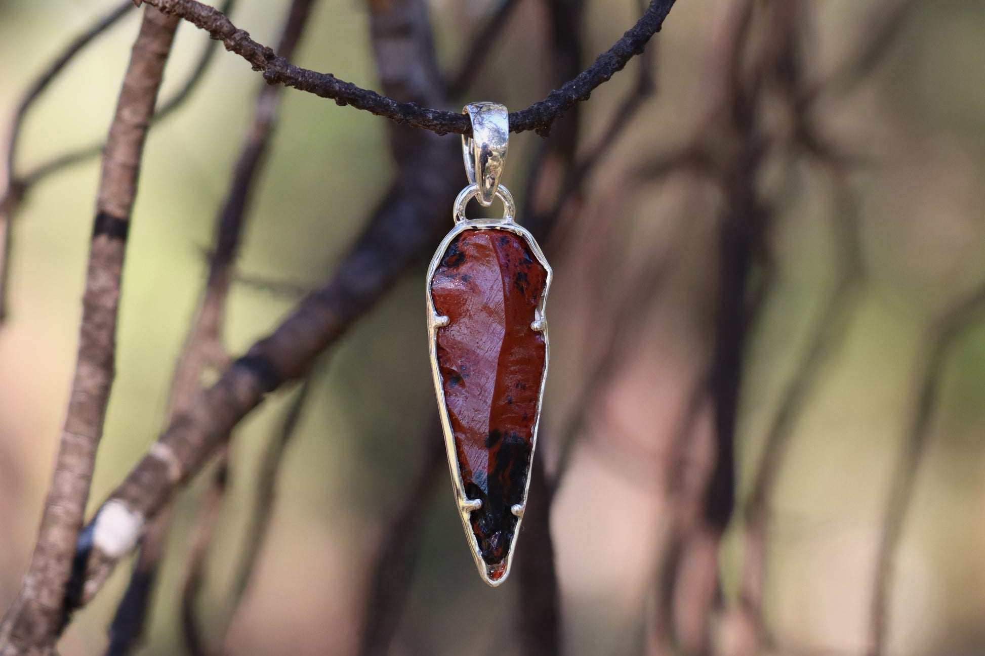 Raw Mahogany Obsidian Pendant set in 925 Sterling Silver, symbolizing protection and grounded energy; photographed outdoors on a branch.
