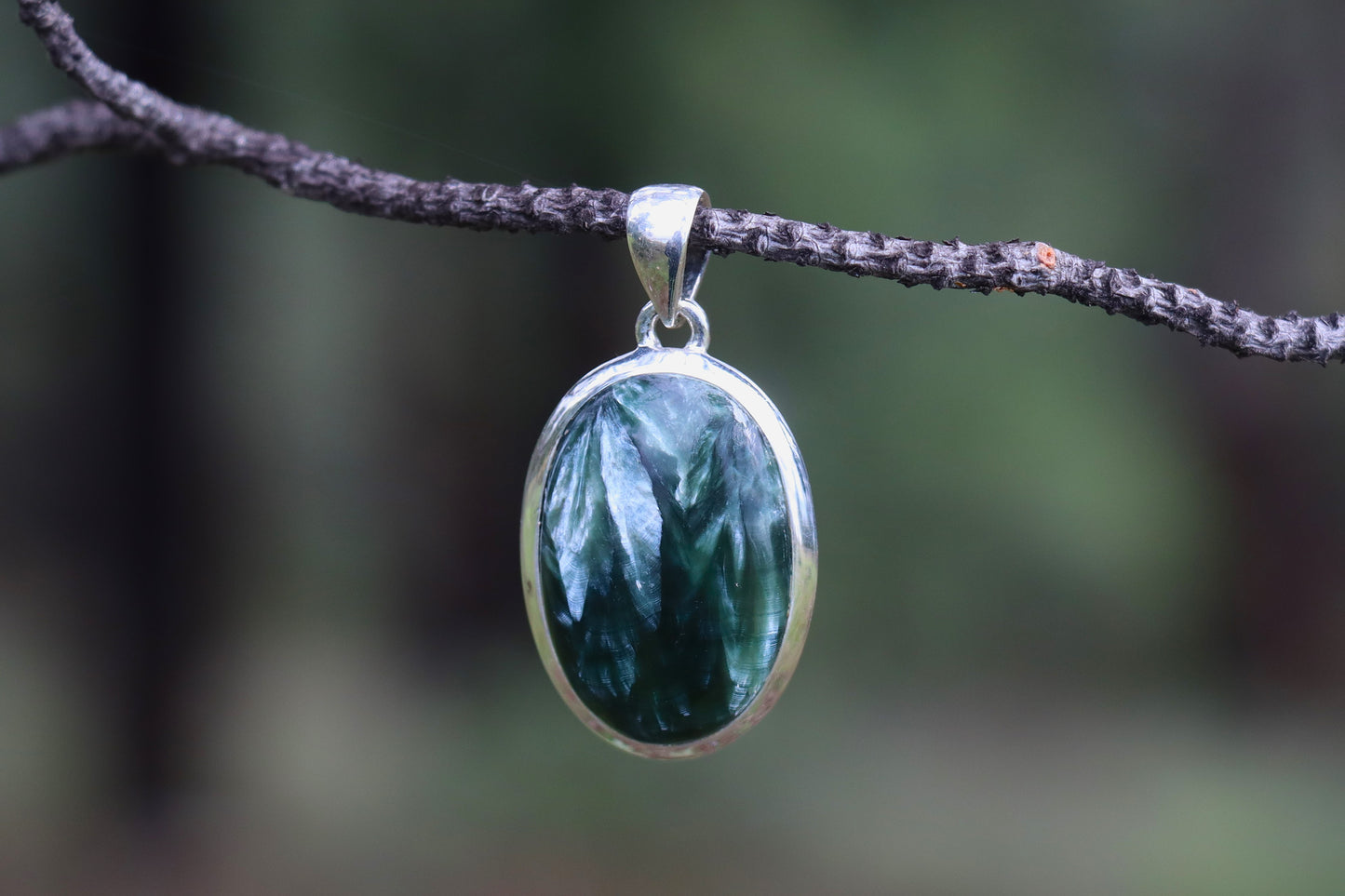 Close-up of a Seraphinite gemstone pendant with detailed silver setting — deep green stone with angelic feather patterns, handmade healing jewelry.