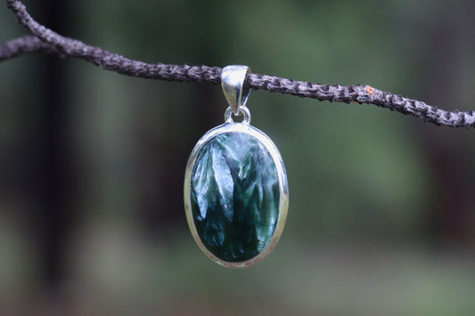 Close-up of a Seraphinite gemstone pendant with detailed silver setting — deep green stone with angelic feather patterns, handmade healing jewelry.