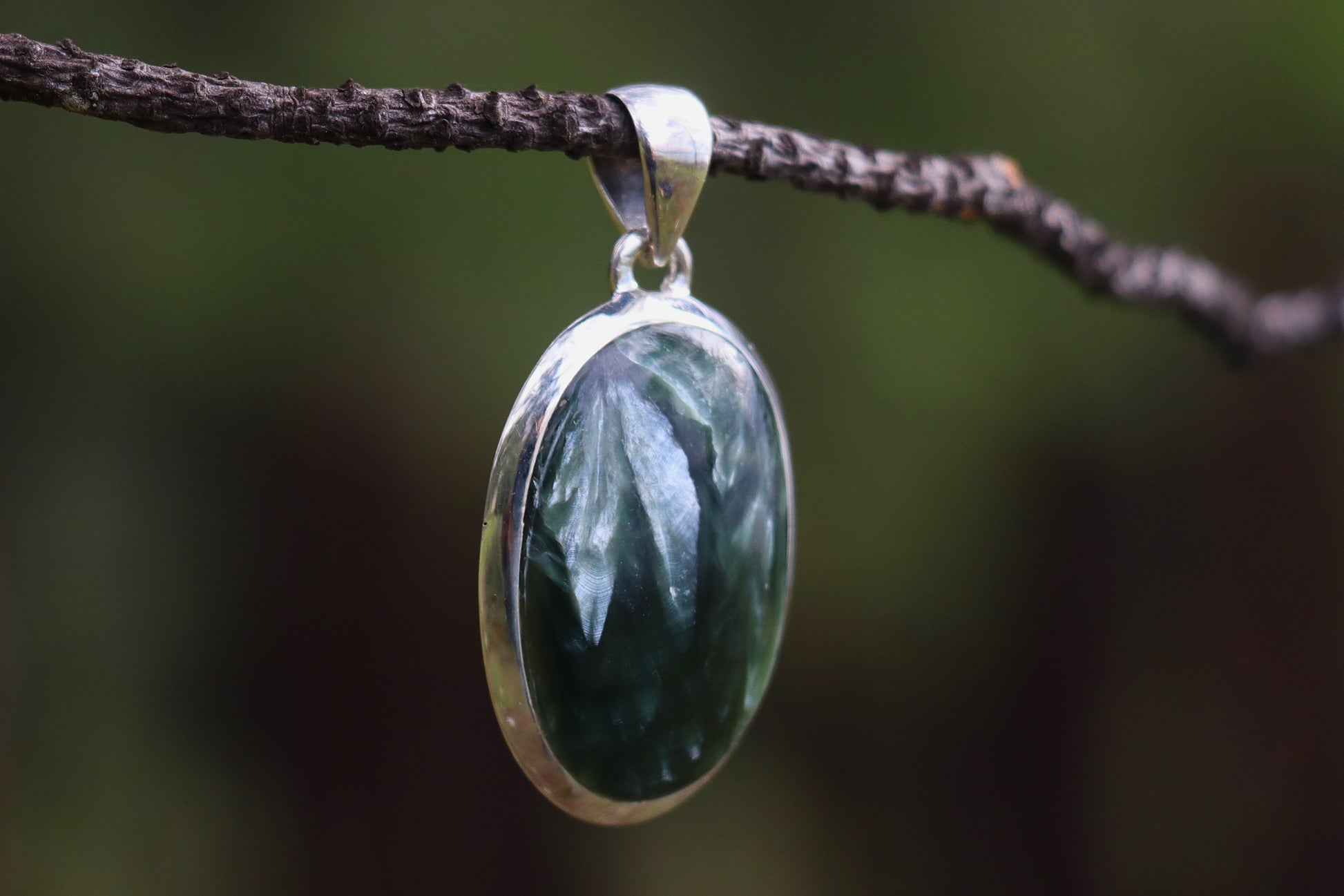 Oval Seraphinite pendant set in sterling silver, showing its green feathery textures. Crystal pendant for emotional restoration, self-care, and energetic balance.