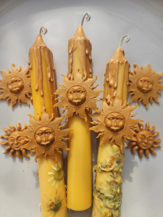 Handcrafted solar energy candle featuring pressed yellow flowers and a golden sun face charm made of wax.