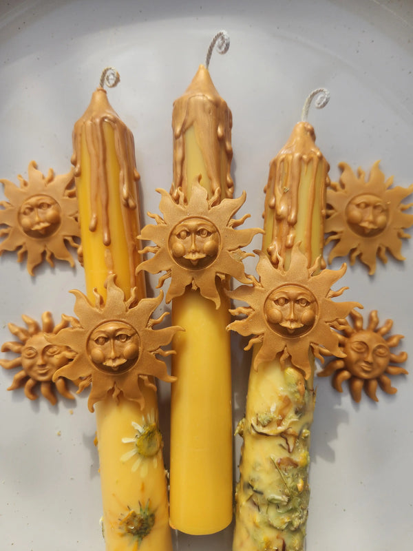 Handcrafted solar energy candle featuring pressed yellow flowers and a golden sun face charm made of wax.