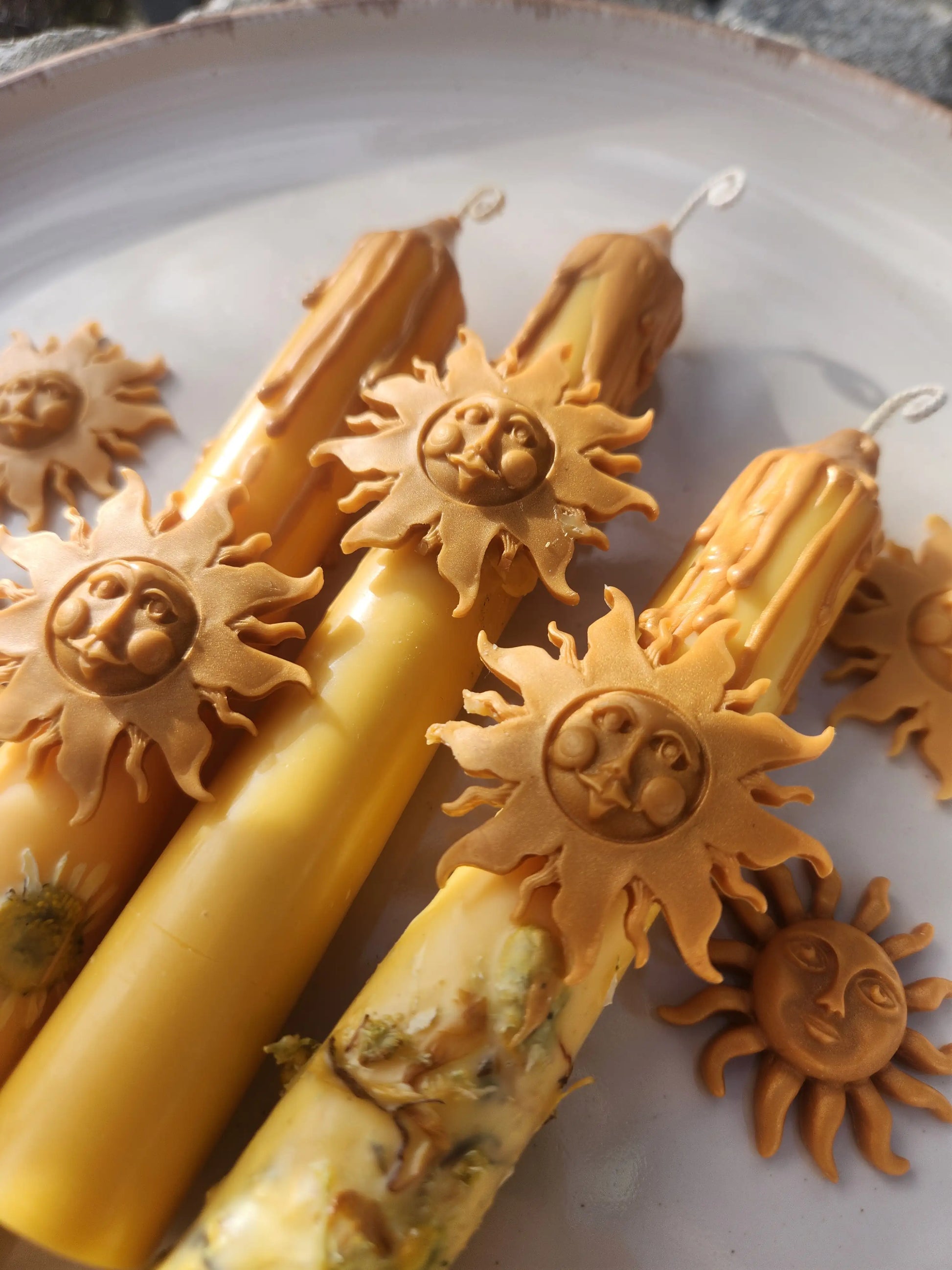 ritual candles with sun charms: one with pressed chamomile flowers, one classic smooth, and one with loose botanical herbs.
